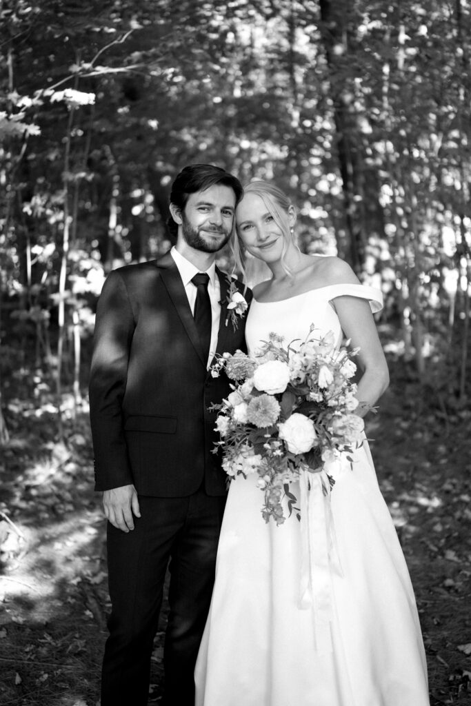 Bride and groom standing in wooded forest with sunlight filtering through trees at Vermont wedding