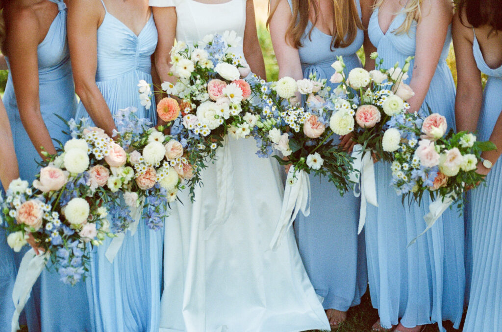 Bride and bridesmaids holding bouquets together on a summer wedding day, photographed on 35mm film