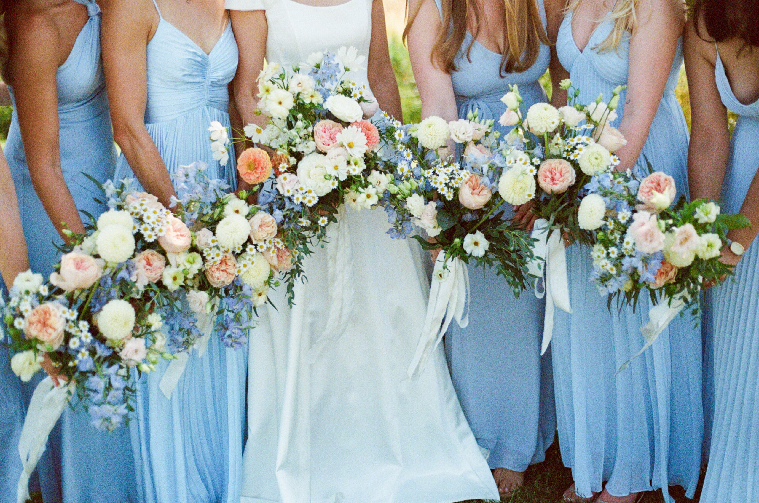 Bride and bridesmaids holding bouquets together on a summer wedding day, photographed on 35mm film