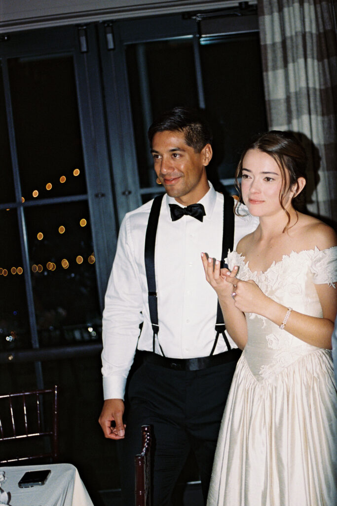 Bride and groom smiling during reception speeches, photographed on 35mm film.