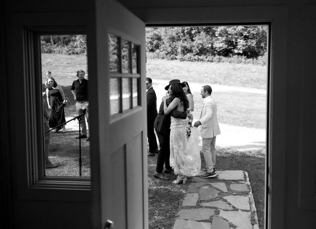 Documentary-style photo of the bride hugging wedding guests seen through a doorway