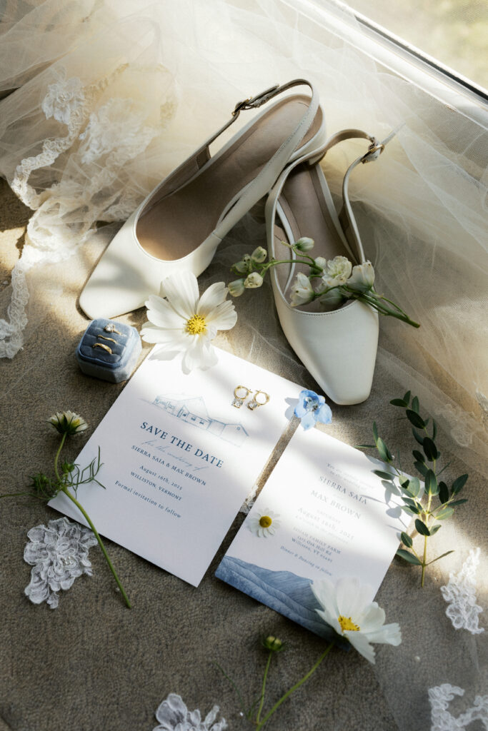 Wedding details including bride's white flats, invitation suite, and seasonal florals arranged in soft light at a Vermont summer wedding