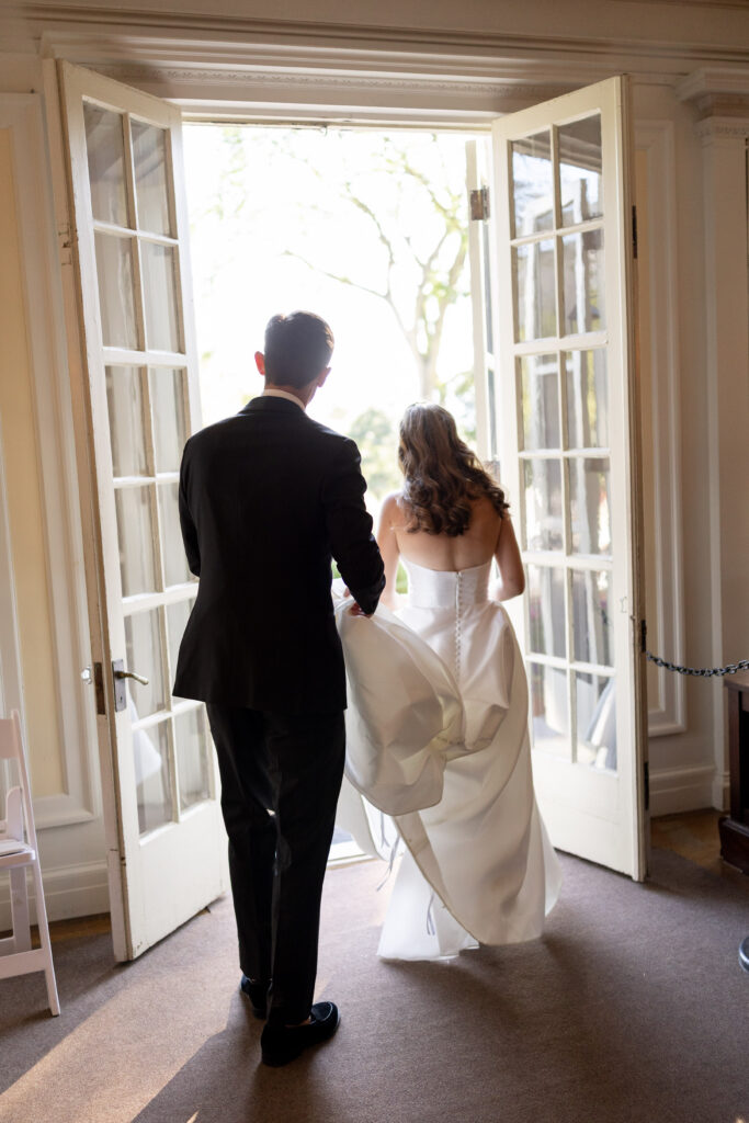 groom walking with bride out mansion doors onto patio at vermont wedding